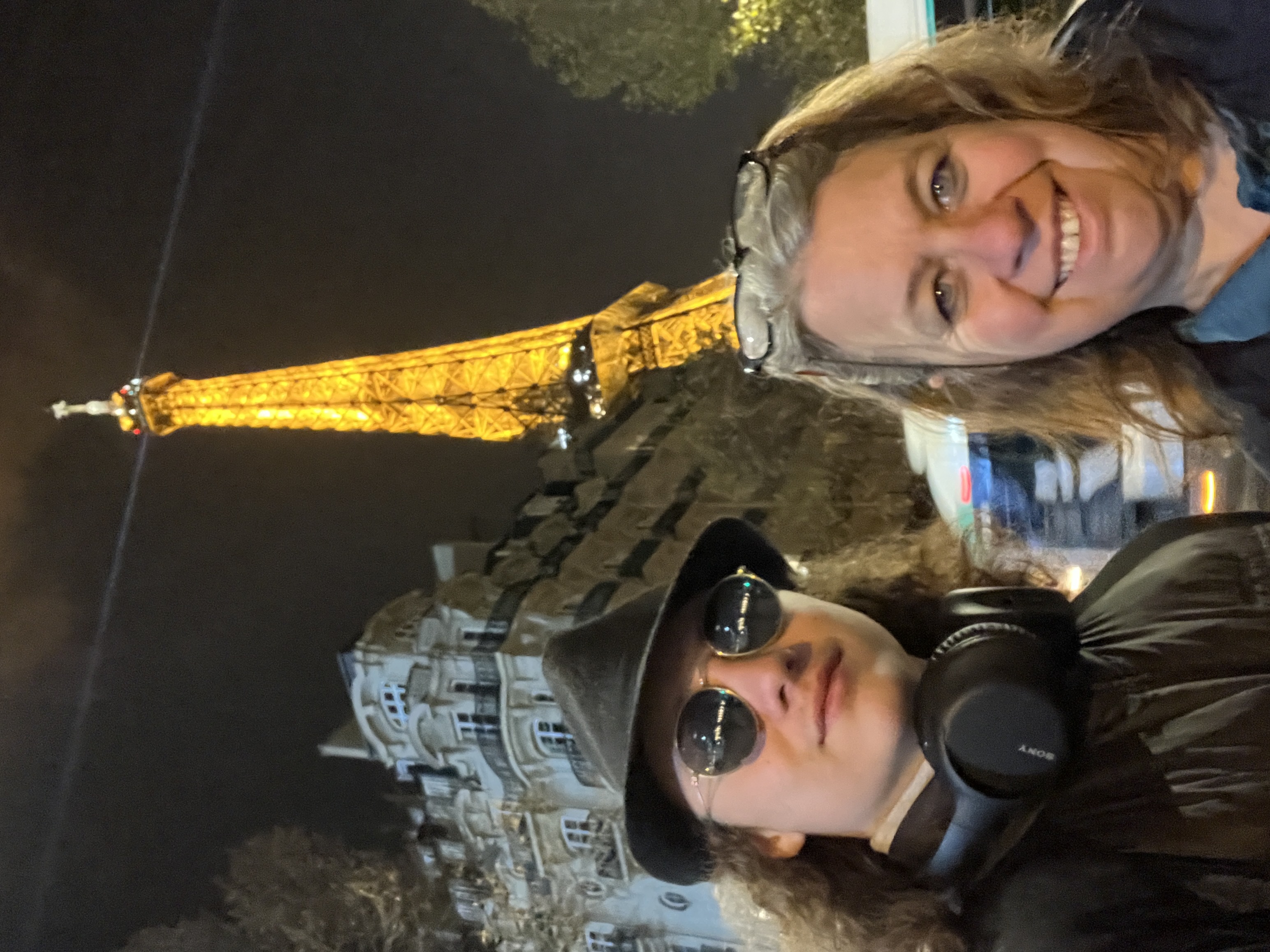 The author and her son standing in front of the Eiffel Tower. It is night and the tower is lit up.