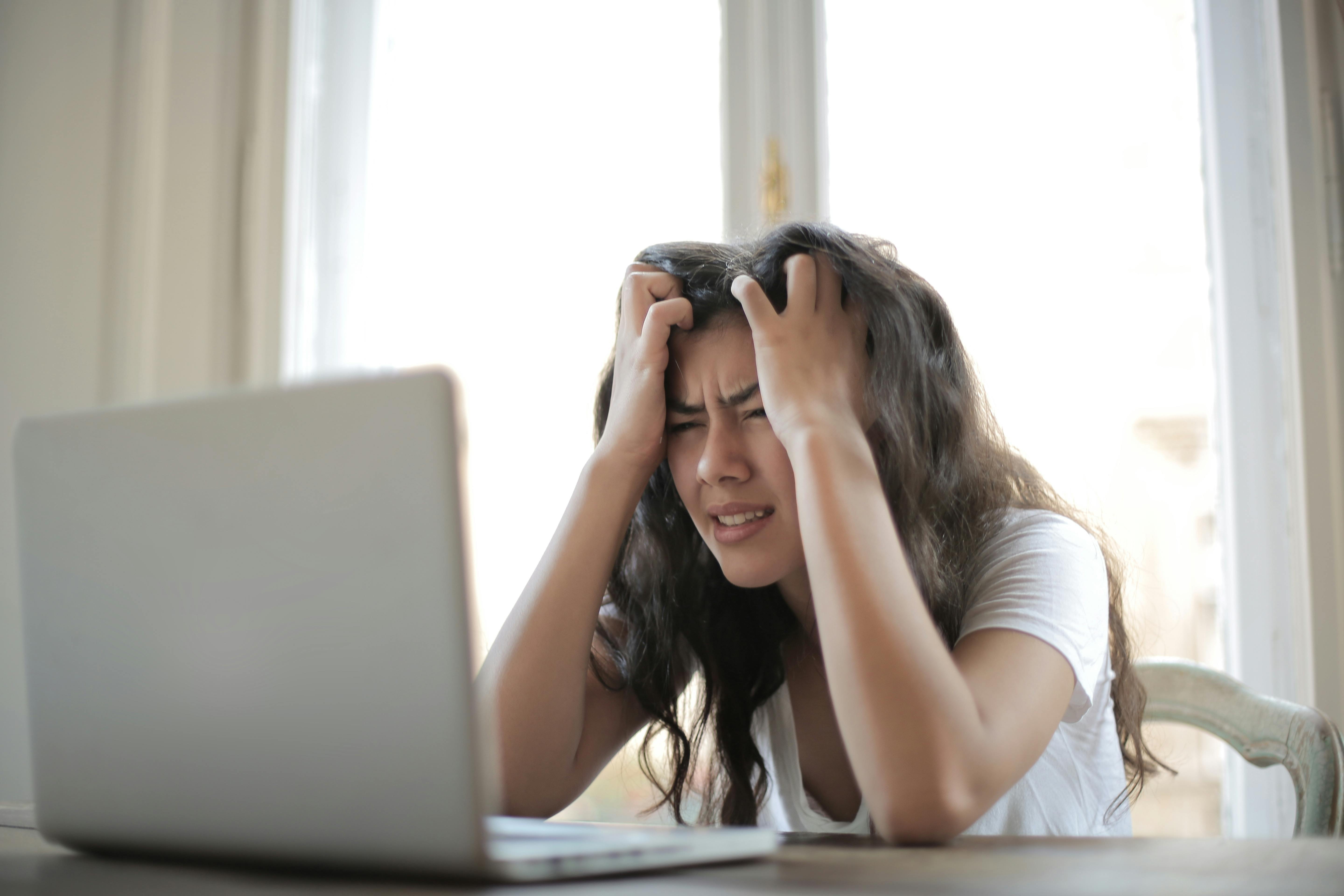 Woman frustrated and holding her hands in her head while looking at a computer.