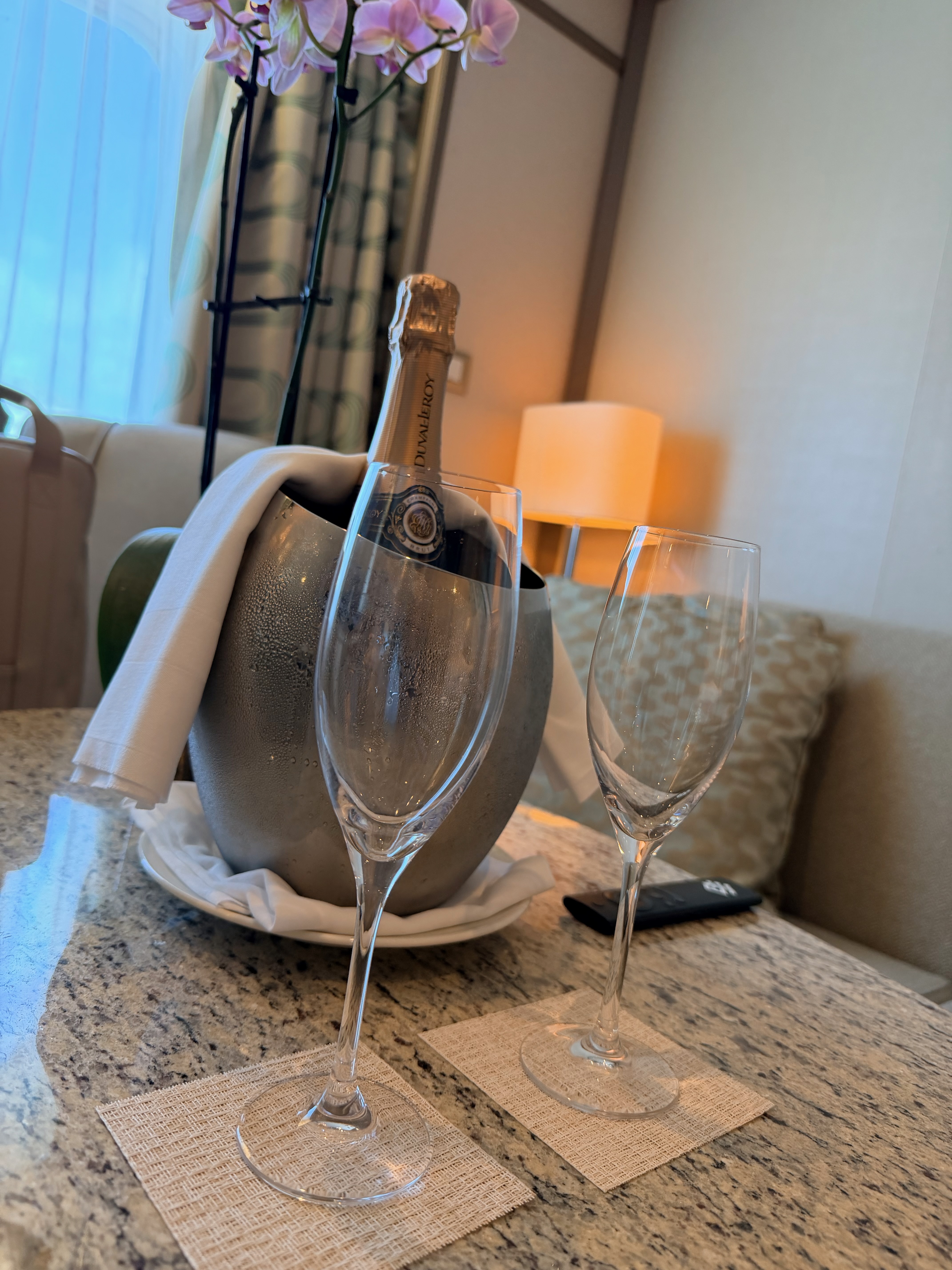 chilled champagne and two champagne flutes waiting on a table with a purple orchid