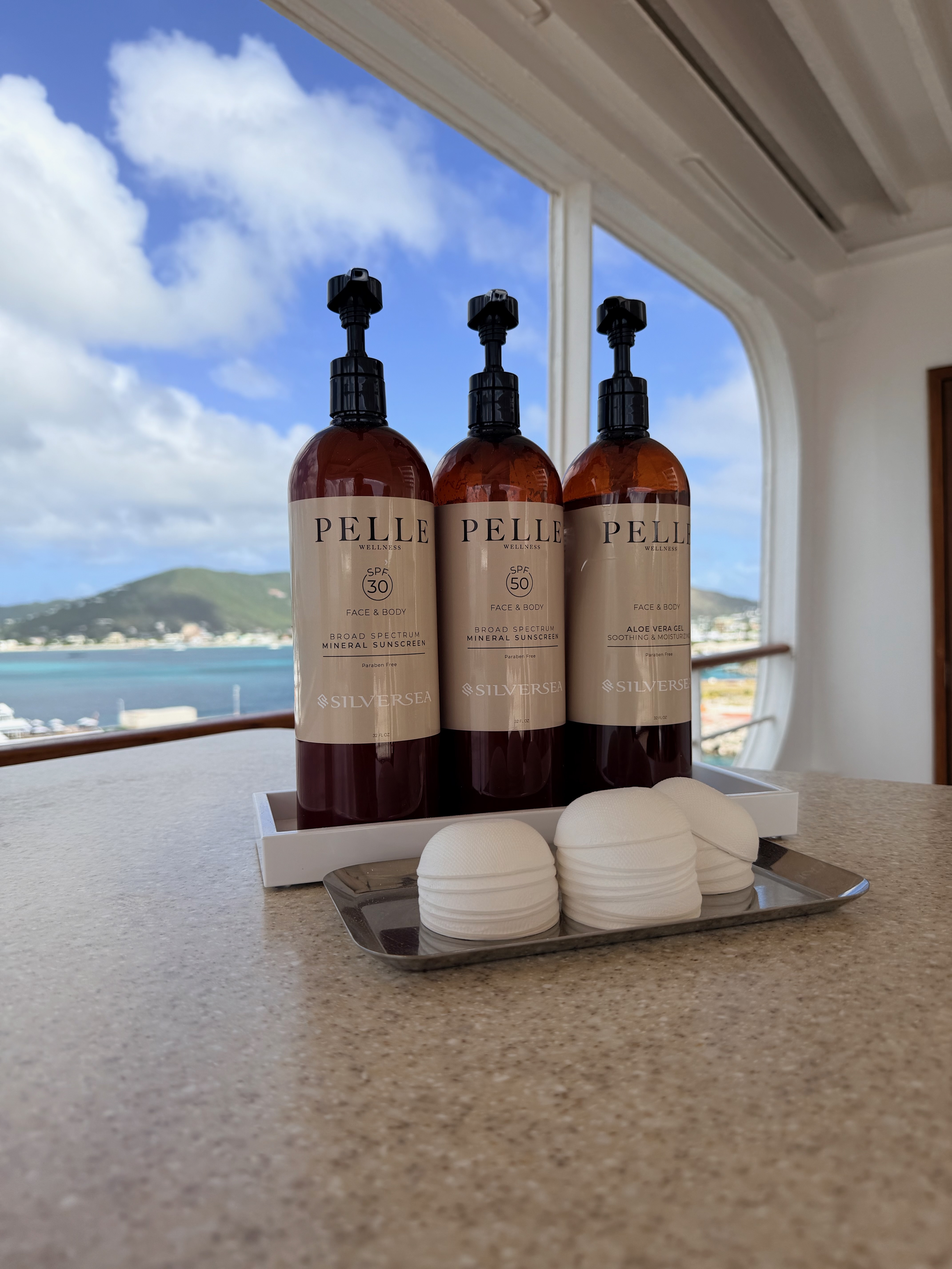image of three bottles of sunscreen and aloe provided on the cruise ship with a Caribbean island in the background