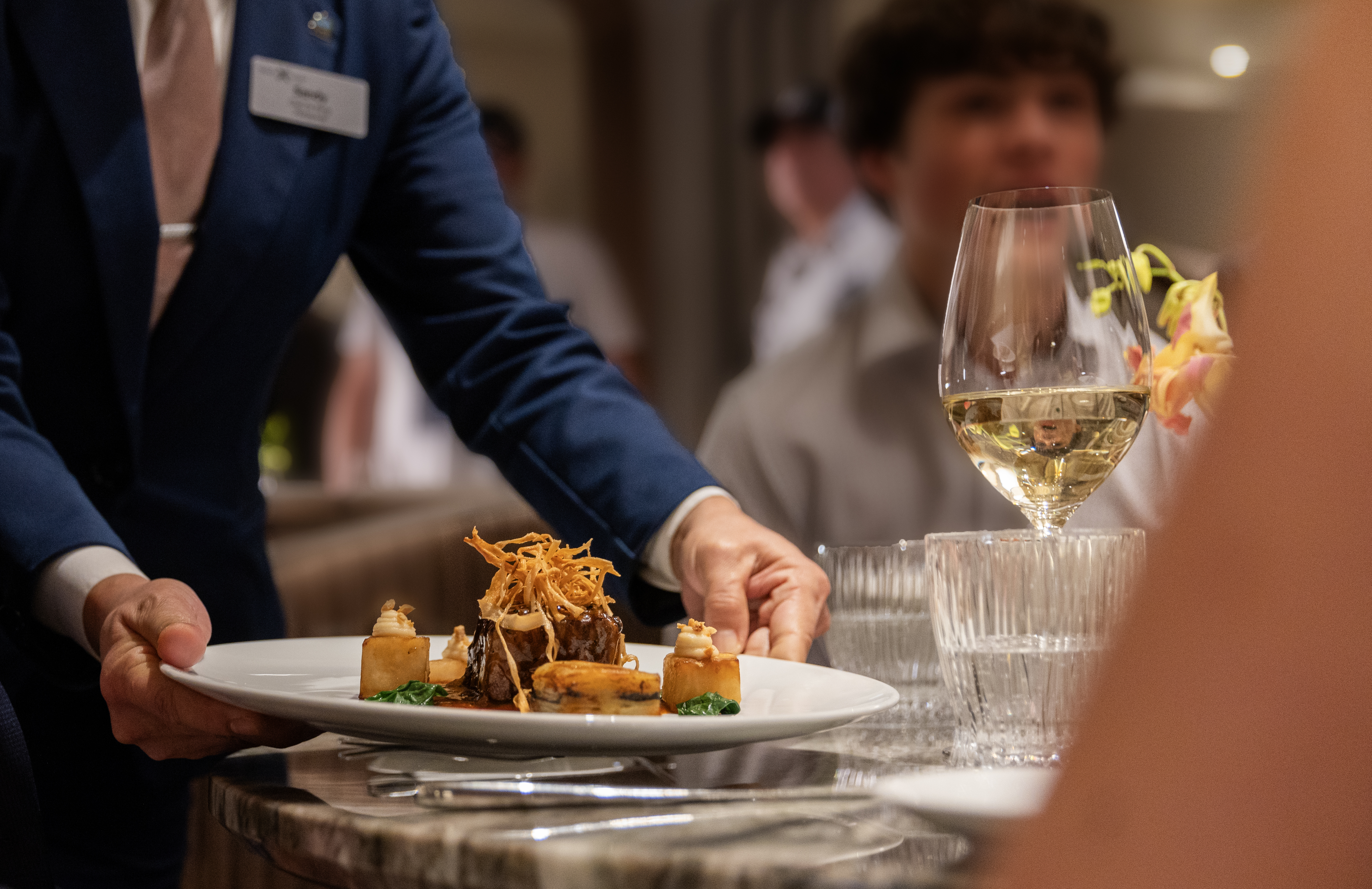A waiter at a fine dining restaurant on board Celebrity Cruises places a plate of delicious food on to the table.